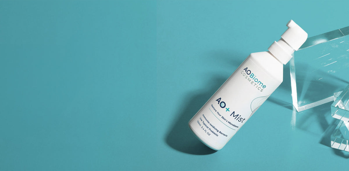 A bottle of AO+ Mist angled diagonally on a solid teal-blue background next to a clear glass block