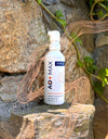 A white pump bottle of AO+ MAX probiotic powder stands on a stone surface outdoors against a rock wall with green ivy