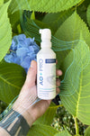 Hand holding a bottle of AO+ PRO against a background of leaves and blue flowers