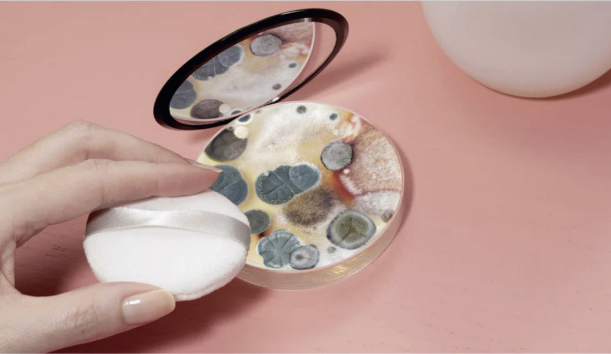 Bloomberg Businessweek photo by Brea Souders of a hand holding a powder puff over an open compact with a petri dish of bacteria versus makeup in it