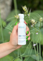Hand holding a bottle of AO+ Mist against a background of leaves and flower buds