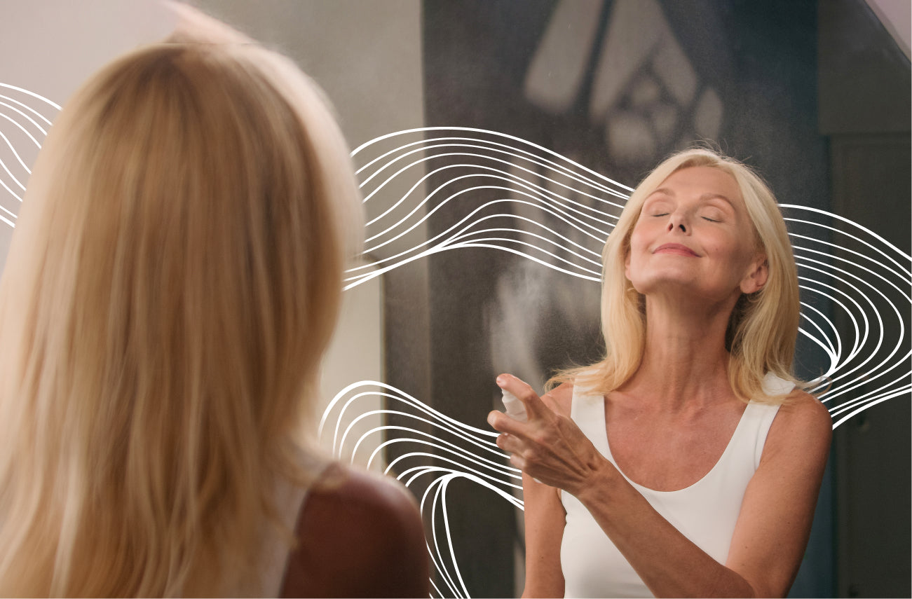 Older woman applying AO+ Mist to her face in front of a mirror with wavy white abstract lines around her.