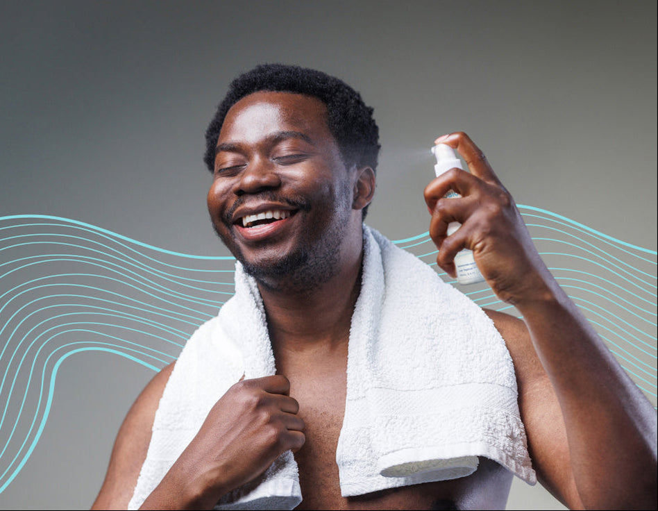A smiling man applying AO+ Mist to his face with a towel around his neck.