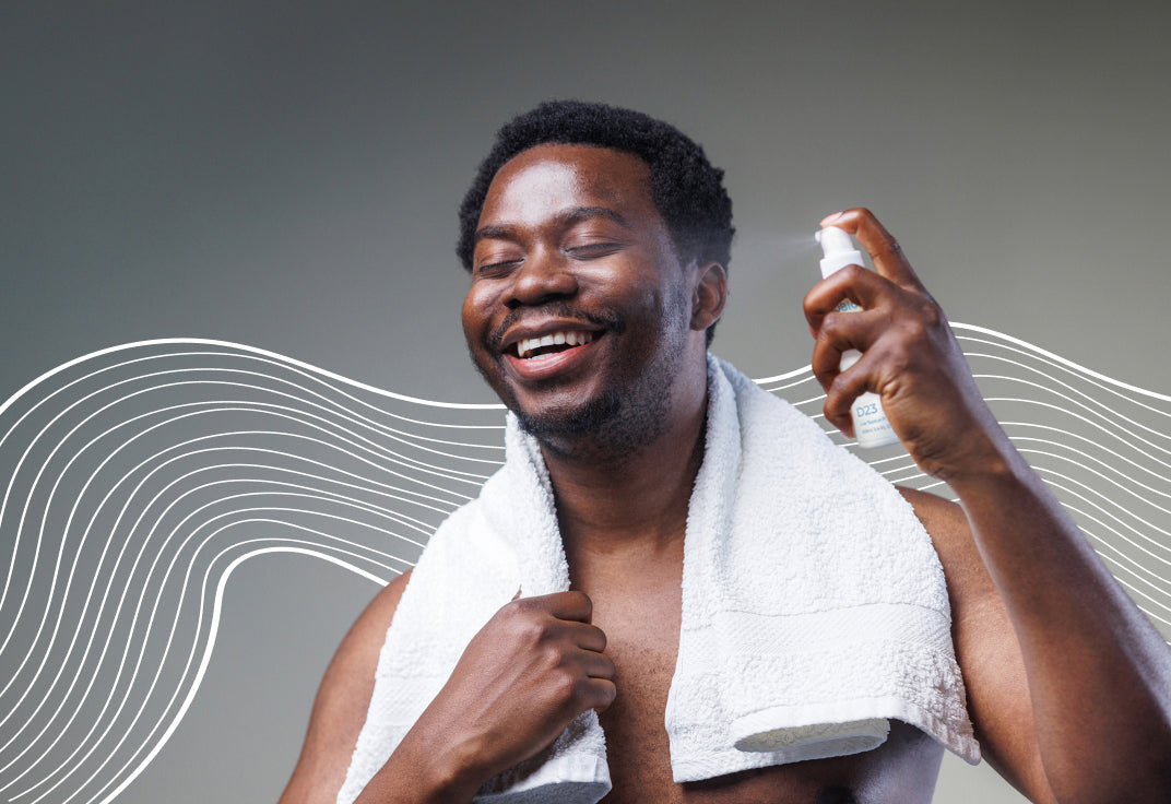 A smiling man applying AO+ Mist to his face with a towel around his neck.