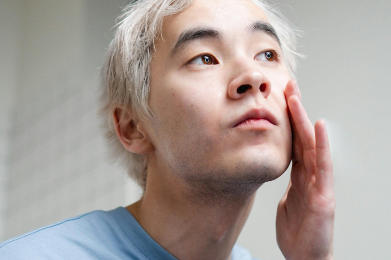 Man with bleached hair touching his cheek with one hand and looking towards a bright light.