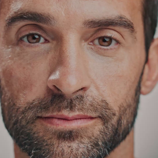 Close-up of a man's face as he closes his eyes and a spray of mist hits each side of his face before he opens his eyes and smiles.